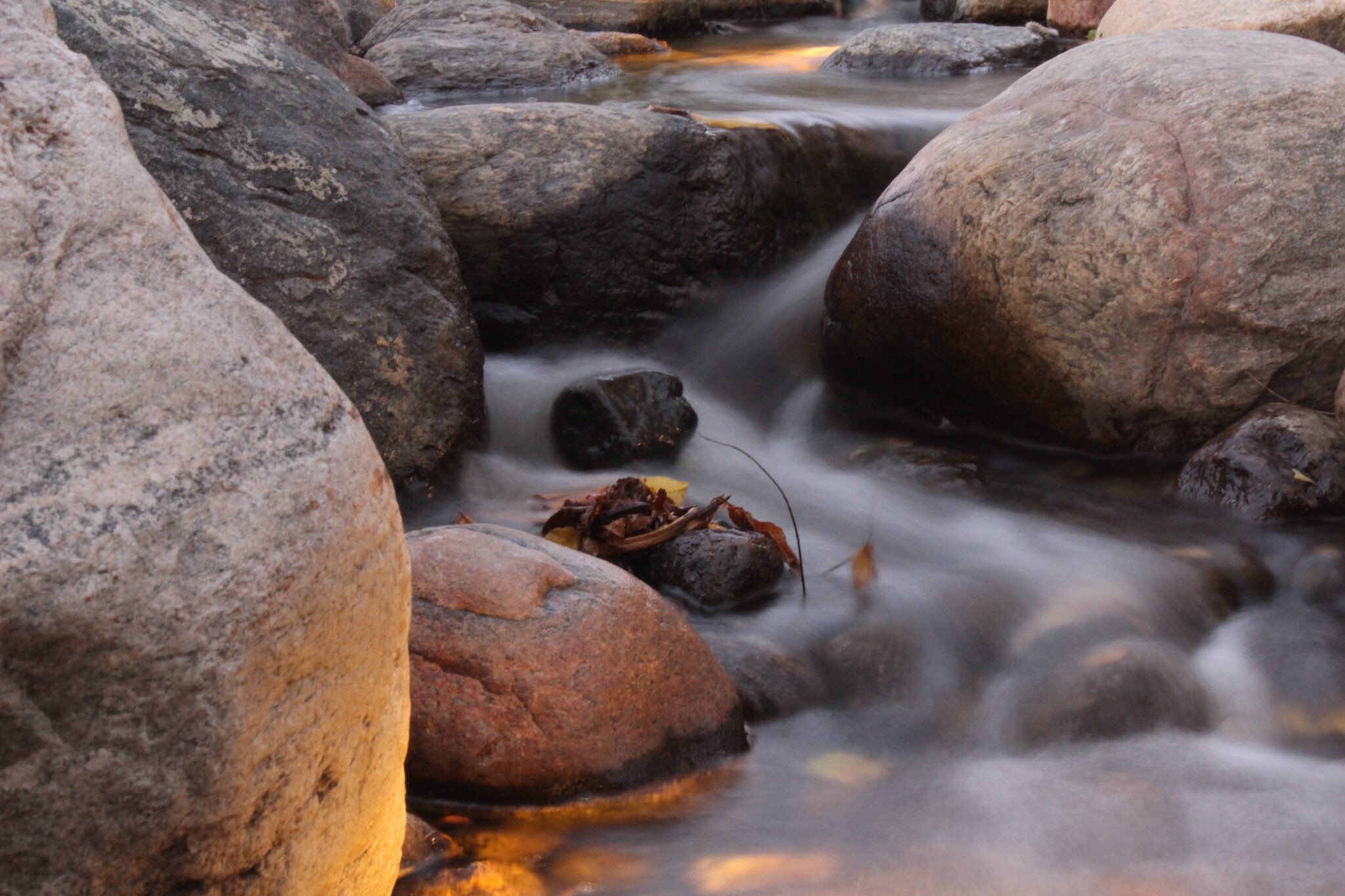 This image captures a serene stream flowing over rocks, with a long exposure creating a smooth, milky effect on the water's surface.