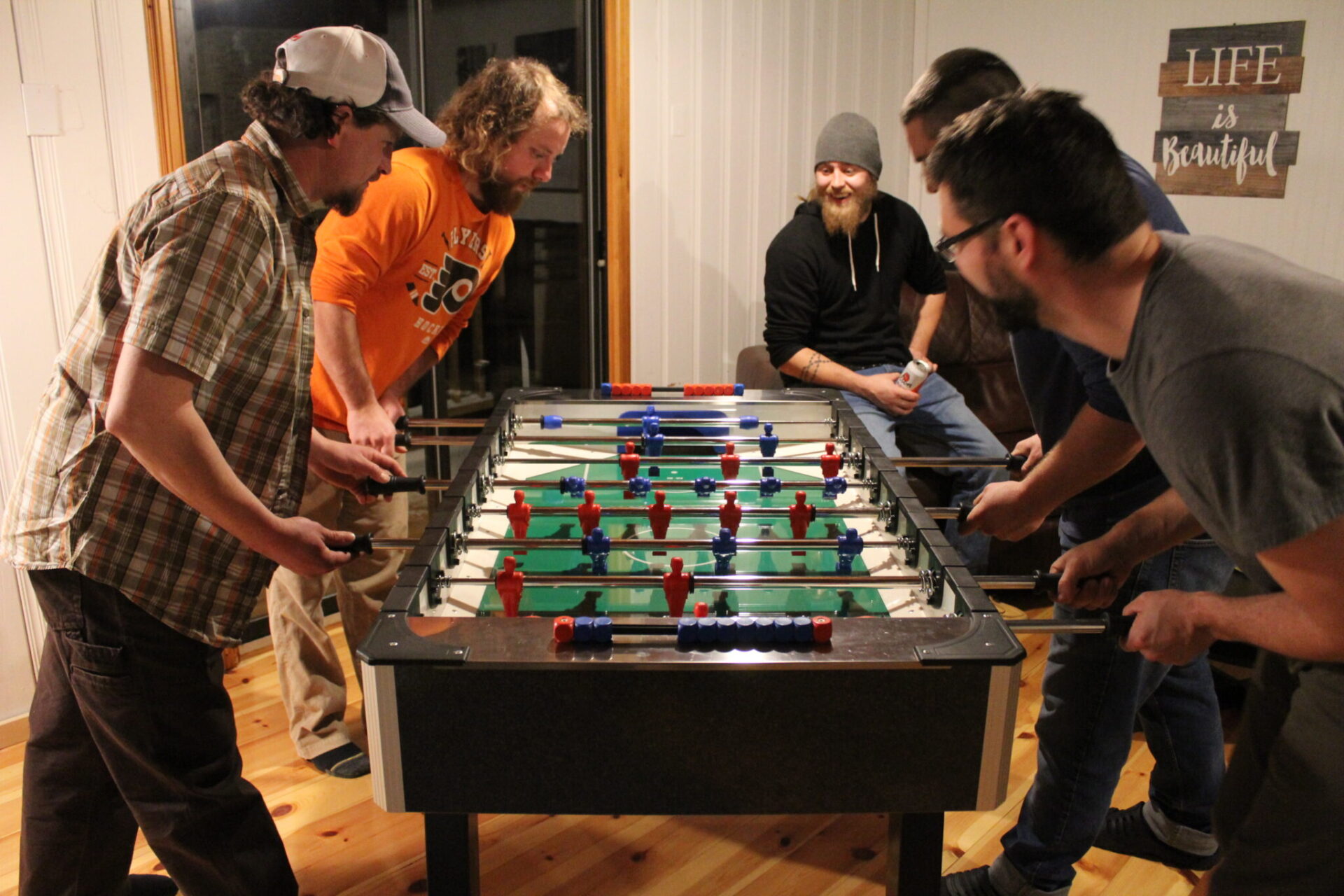 Five people are engaged in a lively game of foosball indoors. The atmosphere appears casual and fun, with everyone intently focused on the game.