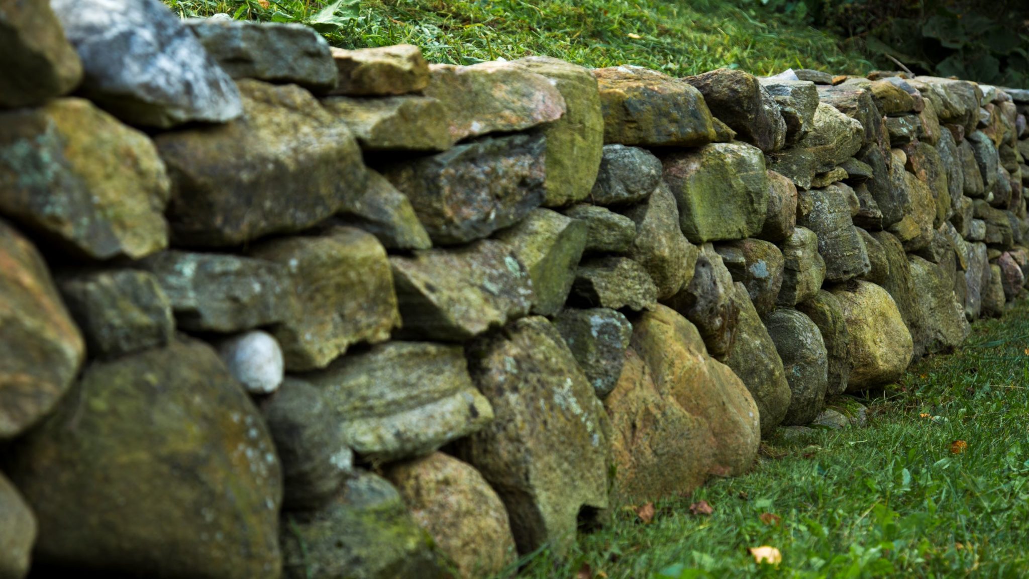 This image shows a rustic stone wall composed of irregularly shaped rocks, surrounded by lush green grass, symbolizing a boundary or enclosure.