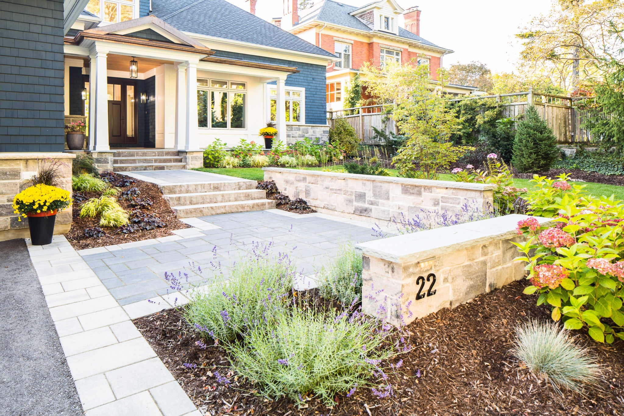 An elegant home entrance featuring a stone pathway, landscaped garden, steps leading to a porch, and clear blue skies. The house number 22 is visible.