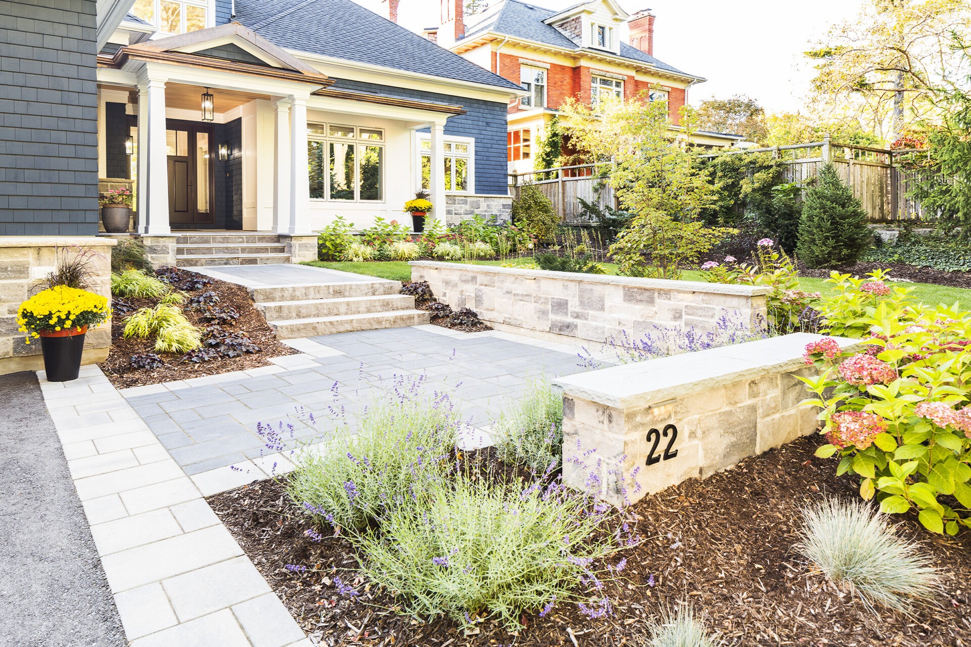 Well-manicured front yard of a stately home with stone steps, colorful plants, and a clear number 22 on a retaining wall.