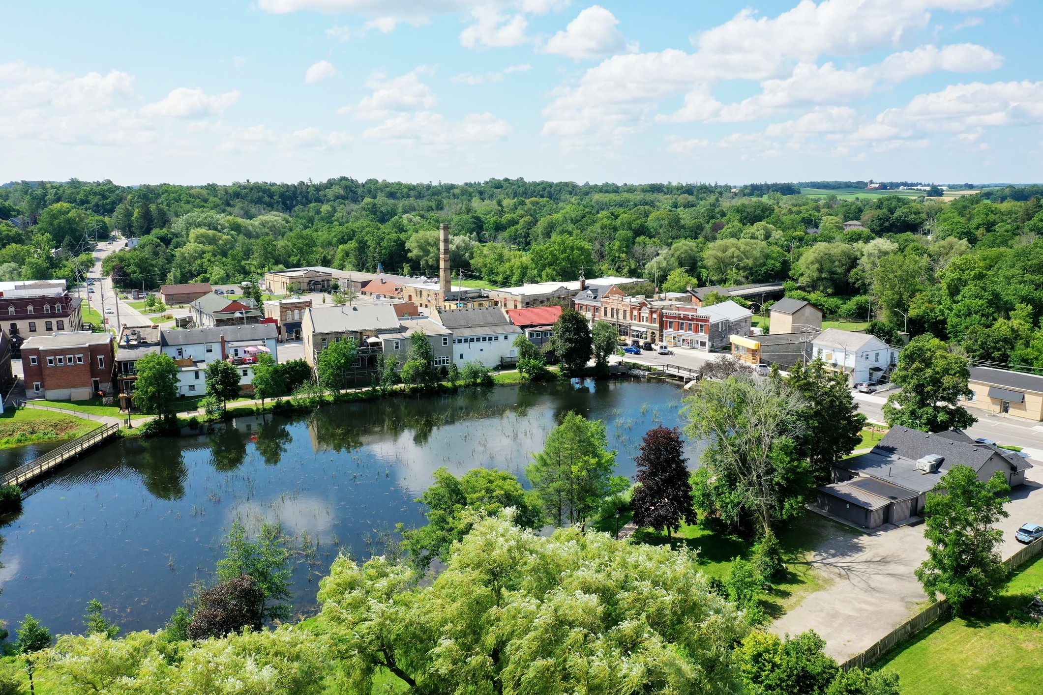 Aerial view of a small town with historic buildings, a river, lush trees, and a blue sky, exuding a serene and quaint atmosphere.