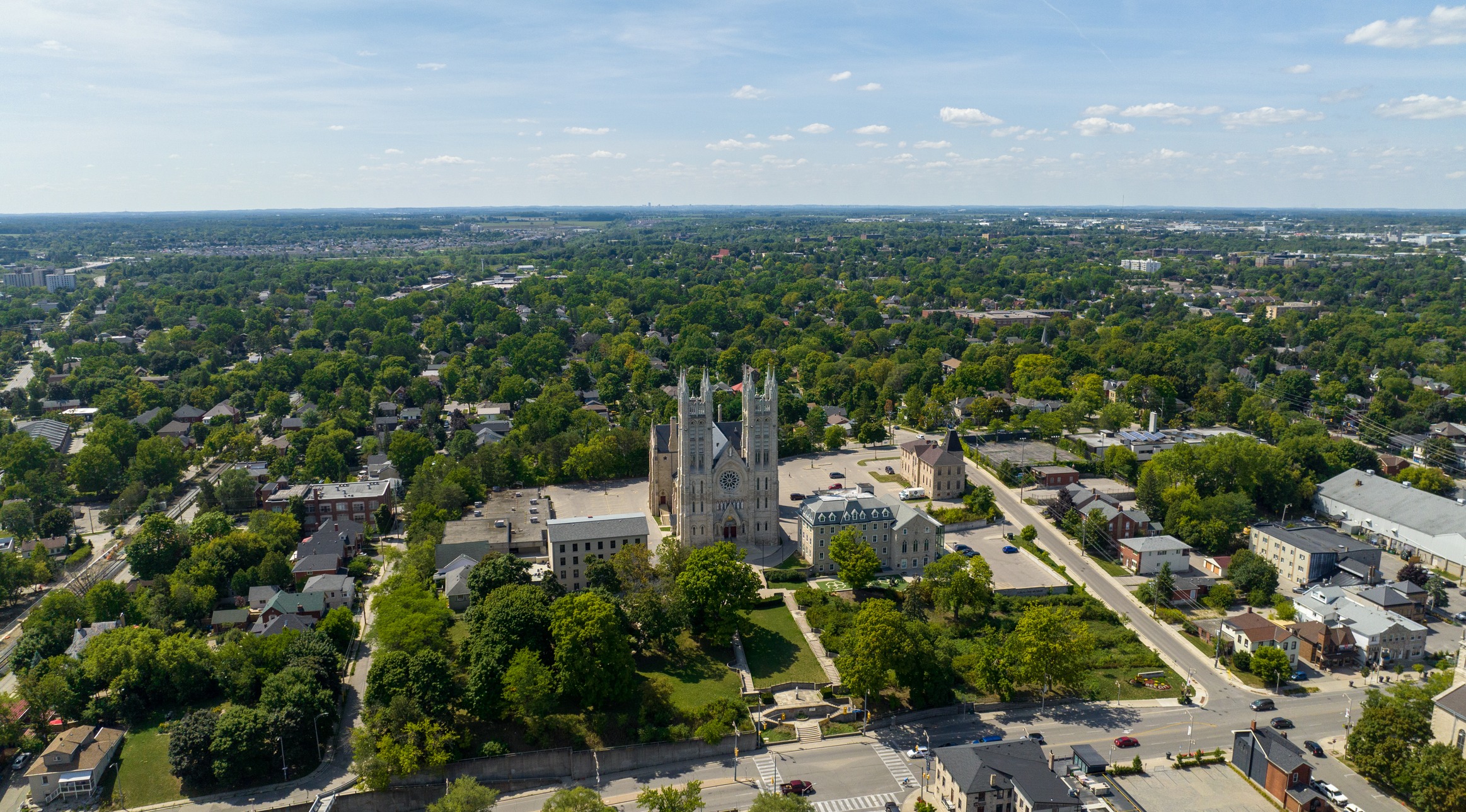 Aerial view of a town featuring a large gothic-style church with twin spires surrounded by green trees, residential areas, and some commercial buildings.