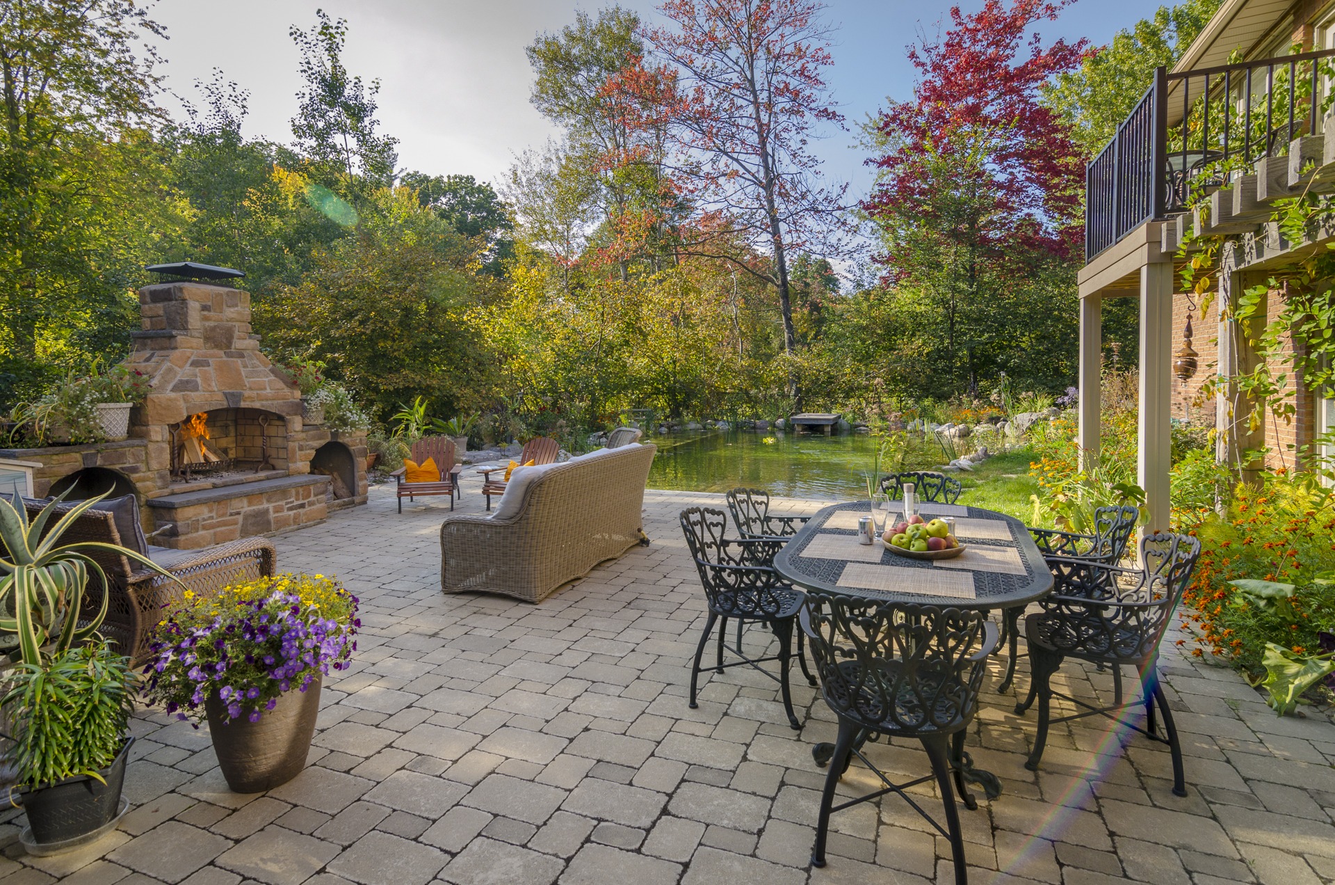 A peaceful garden patio with a stone fireplace, dining table, and surrounding greenery, perfect for relaxing outdoors.