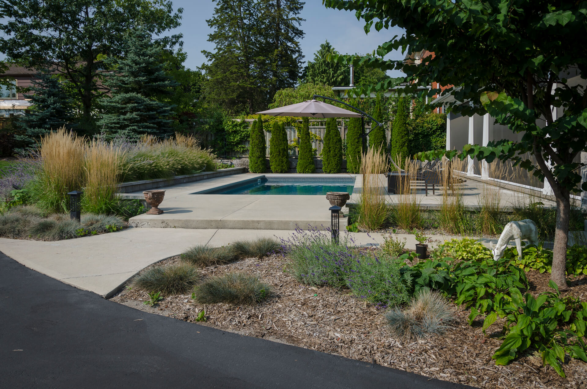 A serene backyard features a swimming pool surrounded by lush landscaping, potted plants, and a patio area with shaded seating, creating a peaceful retreat.