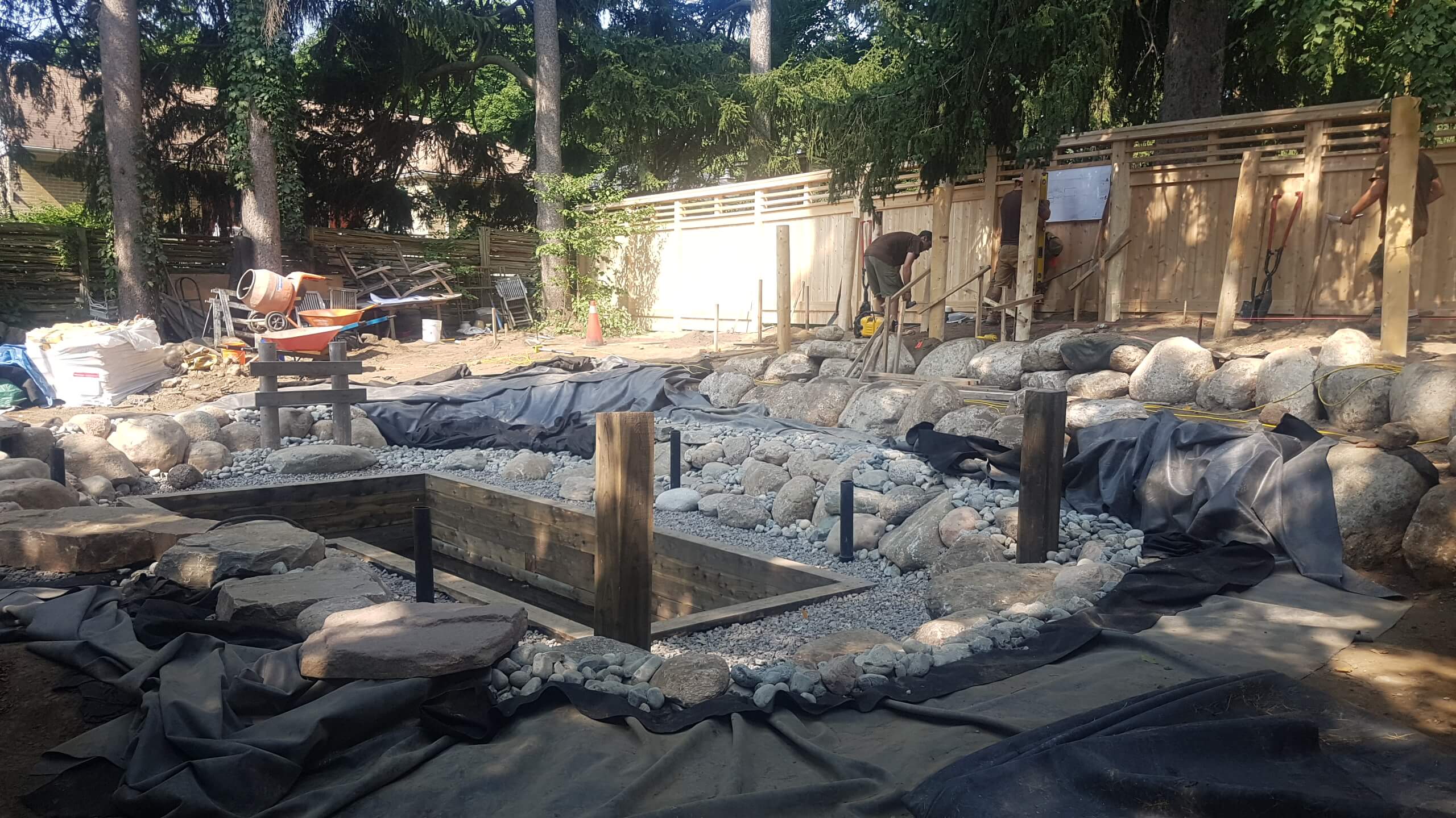 Mid-construction view of the backyard at The Junction in Guelph, showing the natural swim pond layout, rock work, and framing for surrounding landscape elements.