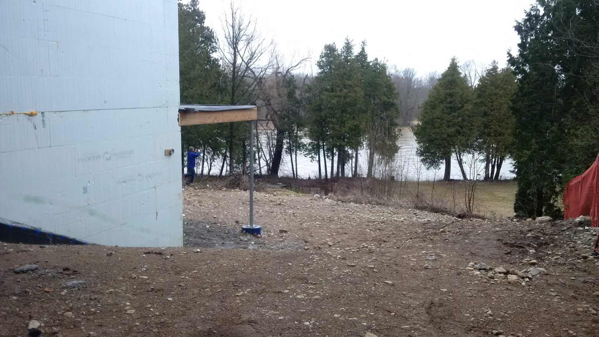 Unfinished backyard beside the house with a steep dirt grade leading toward mature trees and river views