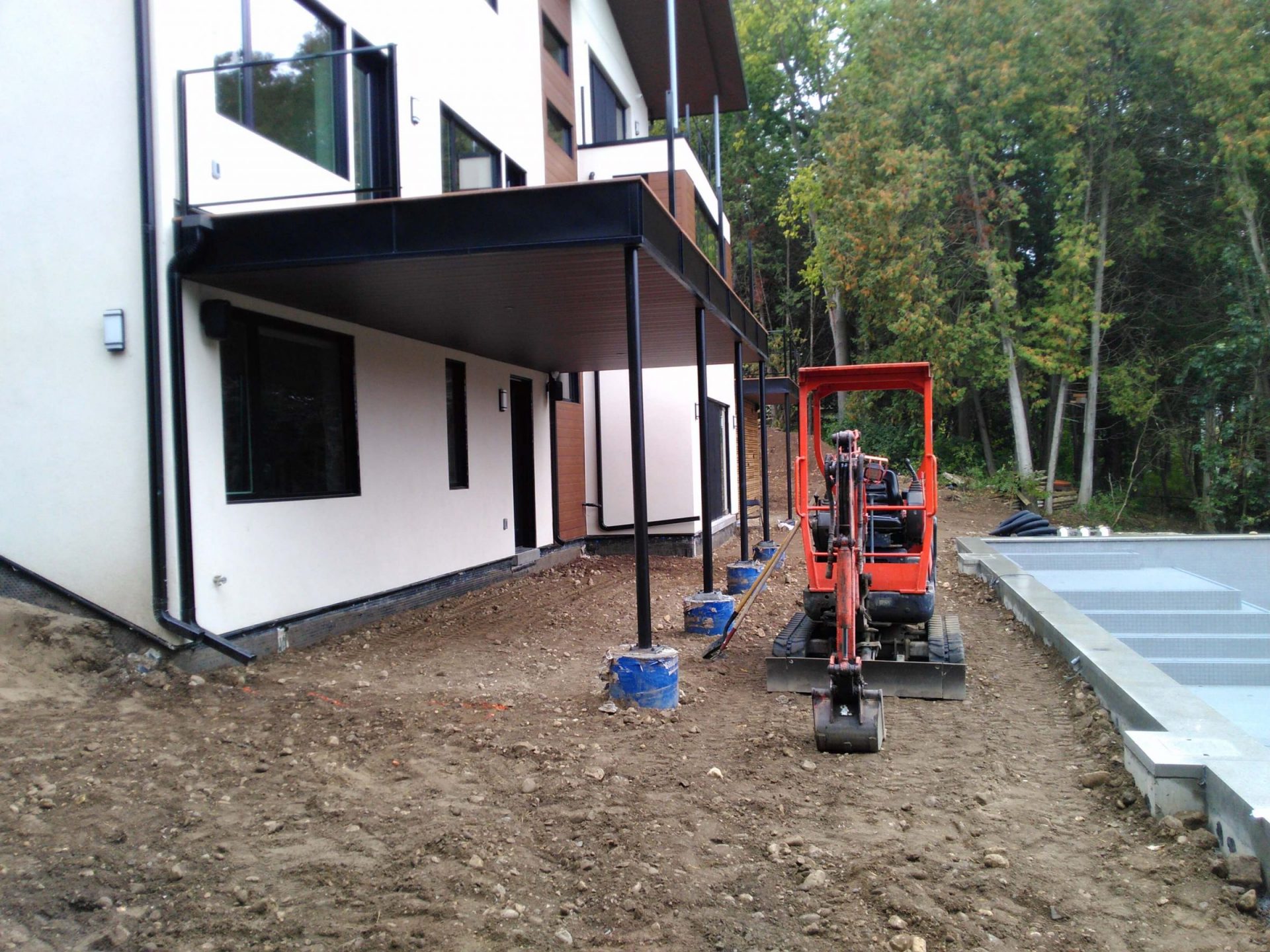 Compact excavator beside the house during backyard construction with pool installation and rough grading underway