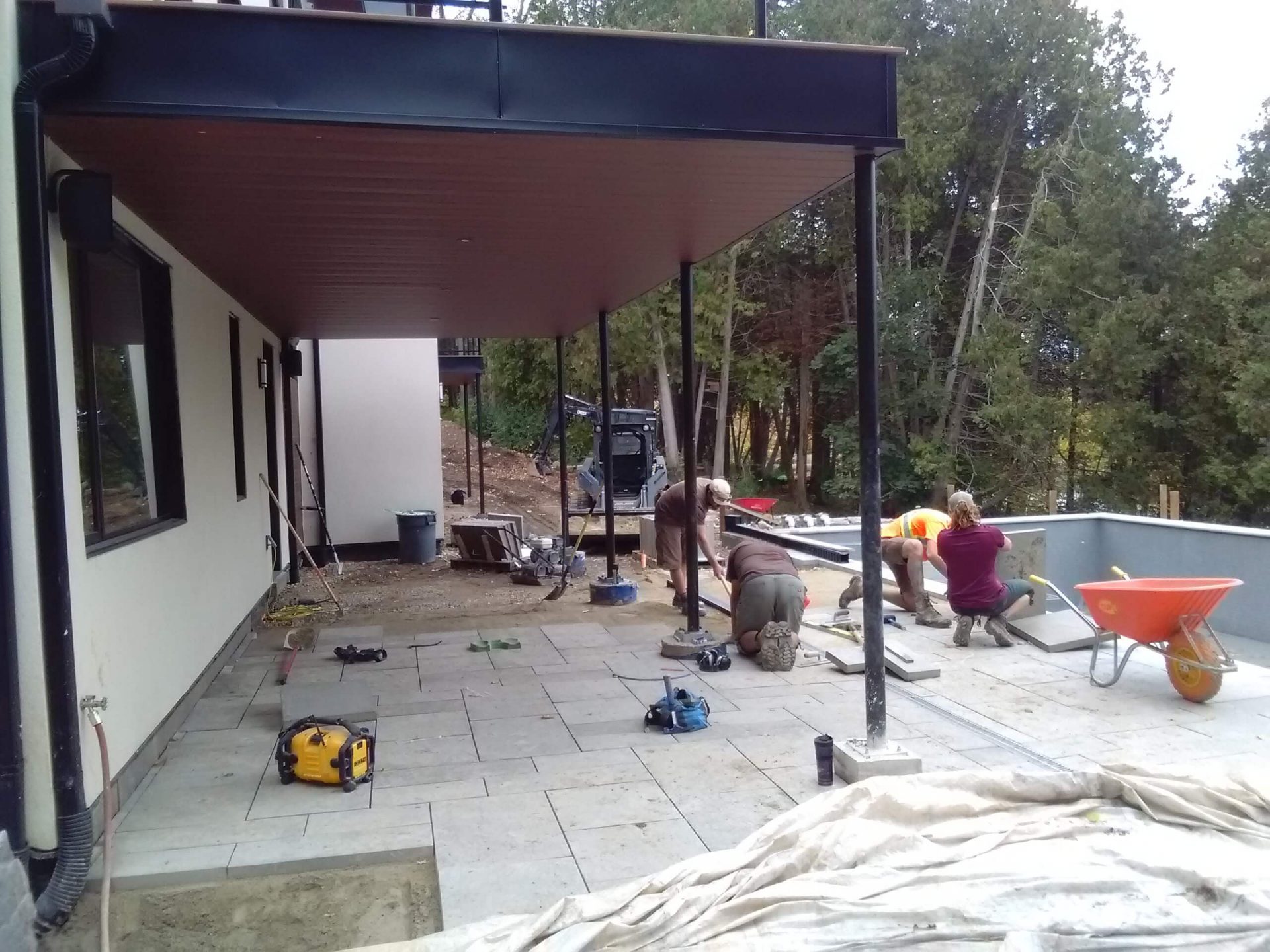 Crew installing large patio pavers under a covered terrace beside the pool during landscape construction
