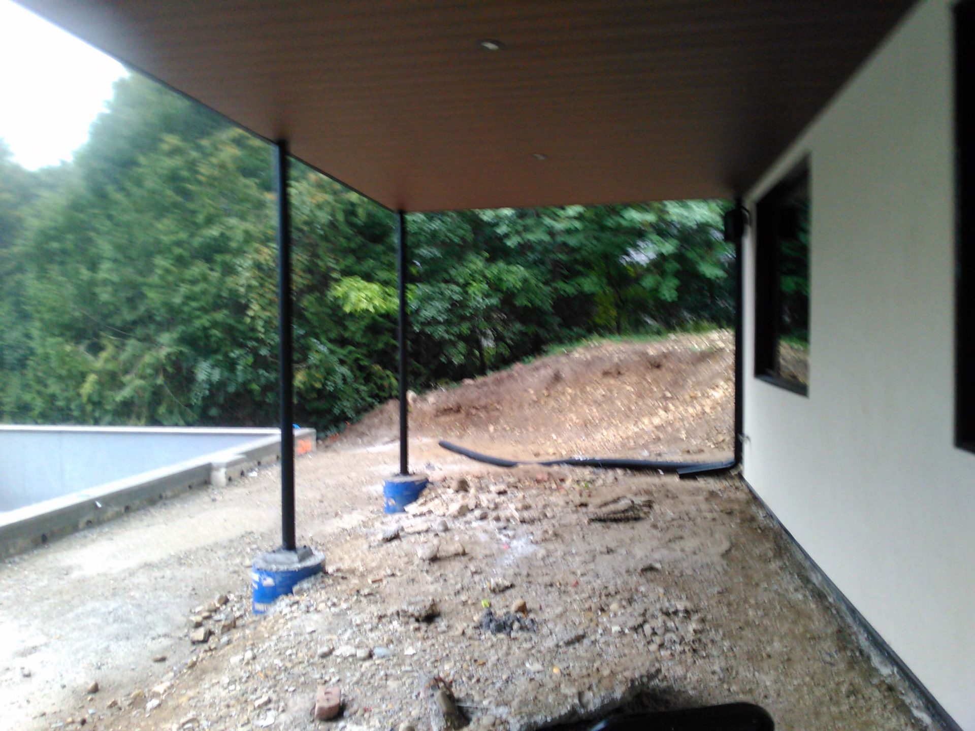 Covered patio area beside the house with muddy ground, exposed grading, and early construction work around the backyard