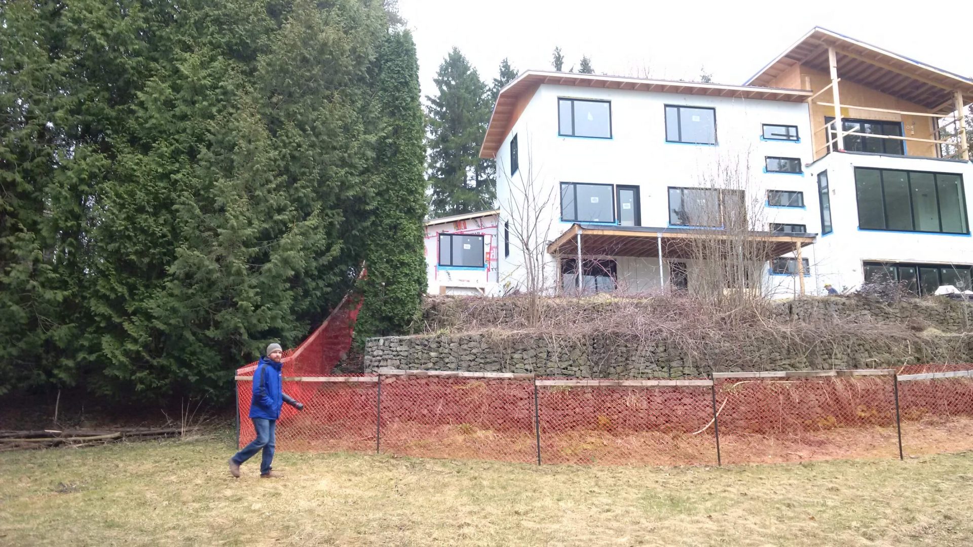 Full rear view of the house on a steep riverside lot with temporary fencing, retaining walls, and unfinished grading