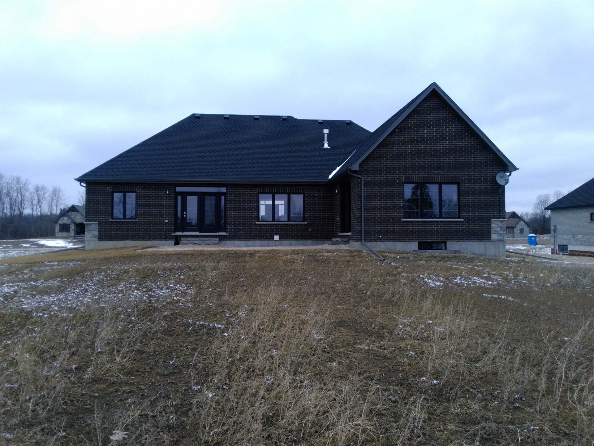 ear view of a new black brick home with an unfinished backyard, rough grass, and no landscaping before construction