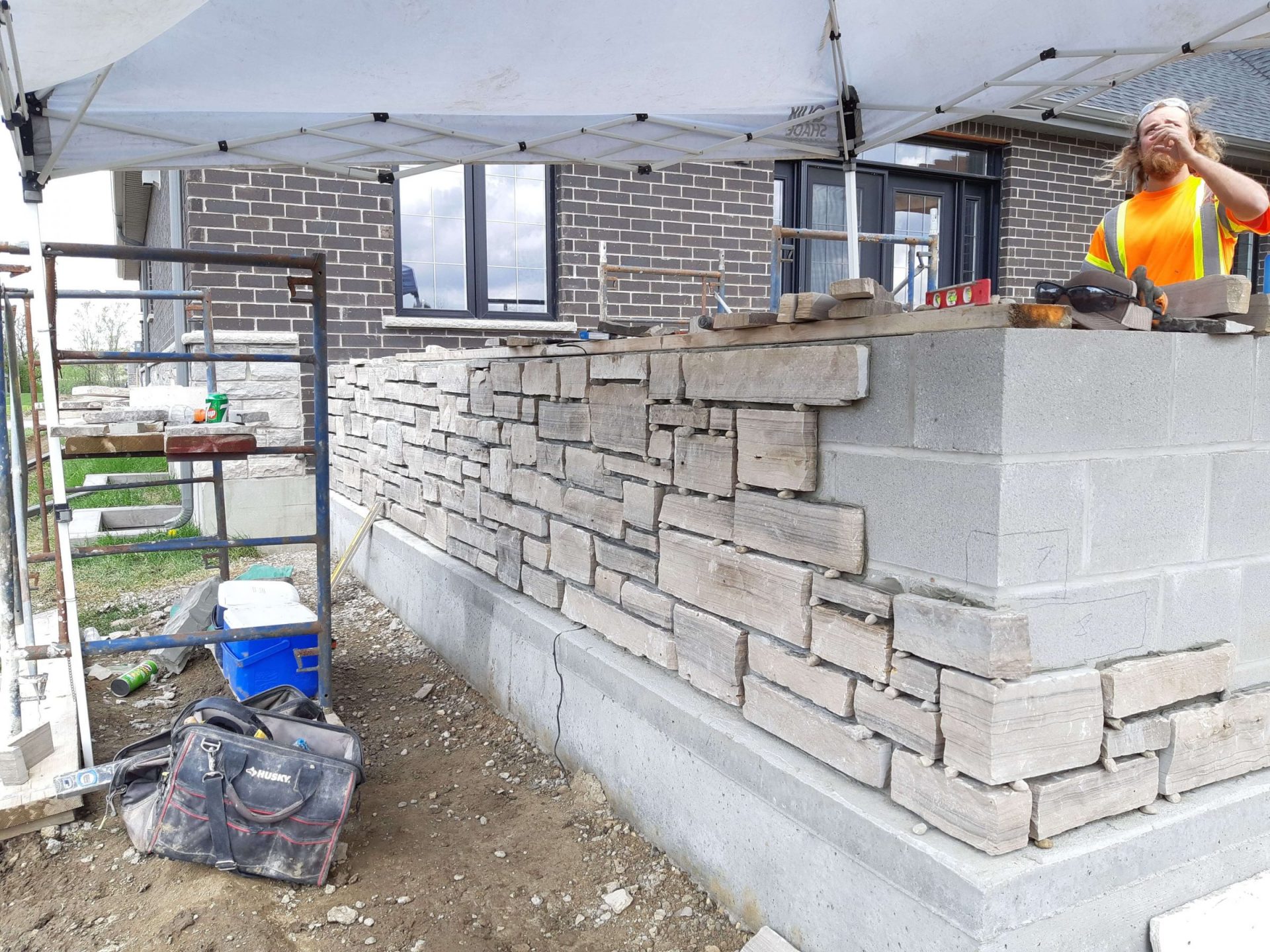 Masonry crew installing stone veneer on a backyard feature wall beside the house during construction