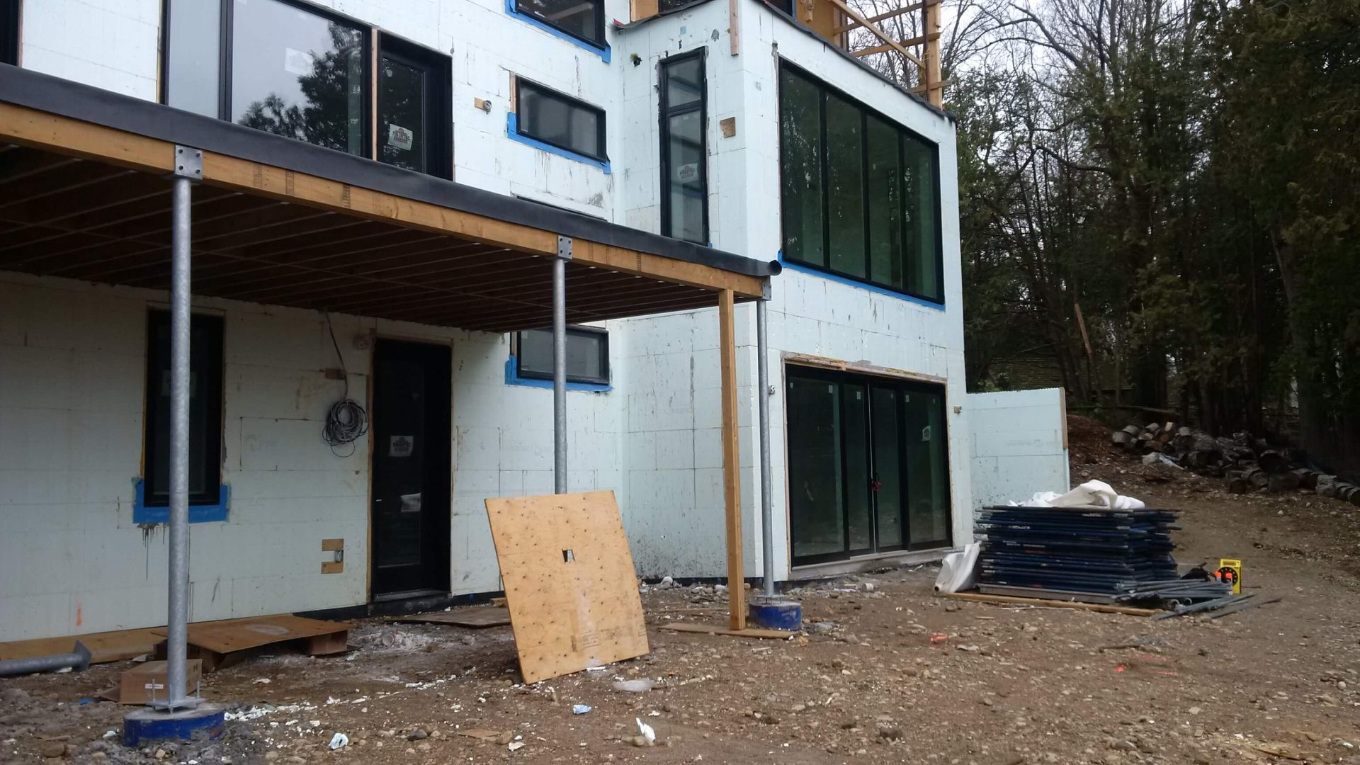 Rear view of a modern home under construction with a covered deck and an unfinished dirt backyard on a sloped lot
