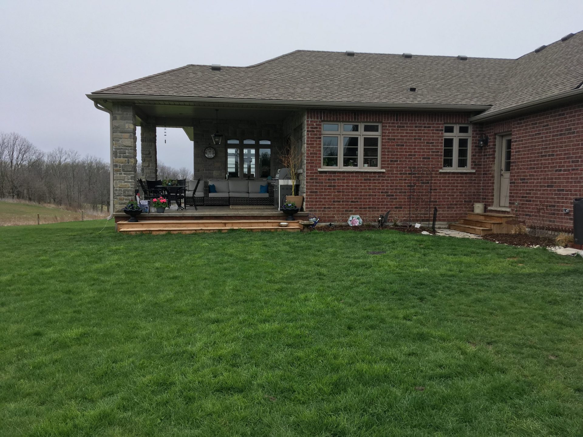 Covered rear patio and open lawn behind a brick house with a simple backyard layout before landscaping