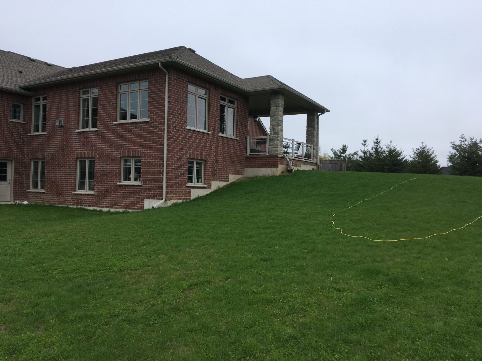 Side view of a brick house with a steep sloped lawn and no defined backyard features