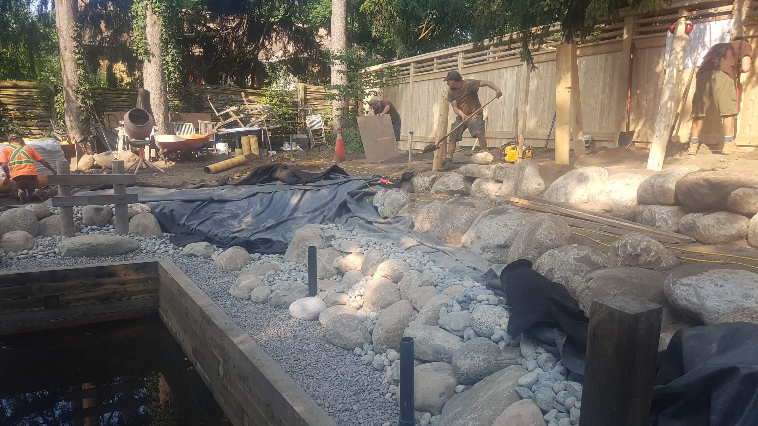 Backyard landscape construction at The Junction in Guelph, showing pond shaping, boulder placement, and the early installation of structural posts.