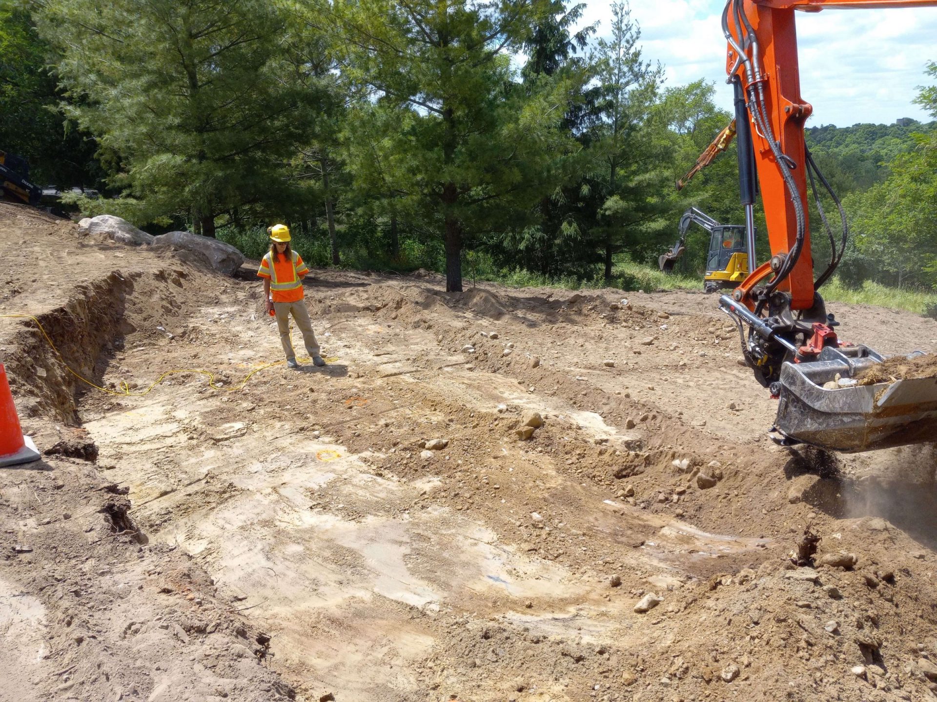 Excavation underway for the plunge pond with a worker and excavator shaping the future water feature in the backyard