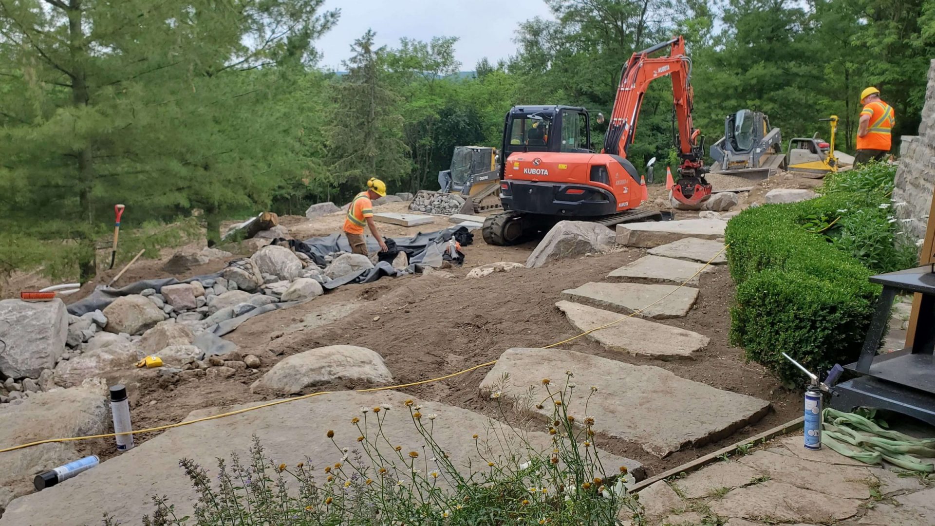 Large natural stone steps, boulders, and stream construction in progress as the backyard layout takes shape beside the house