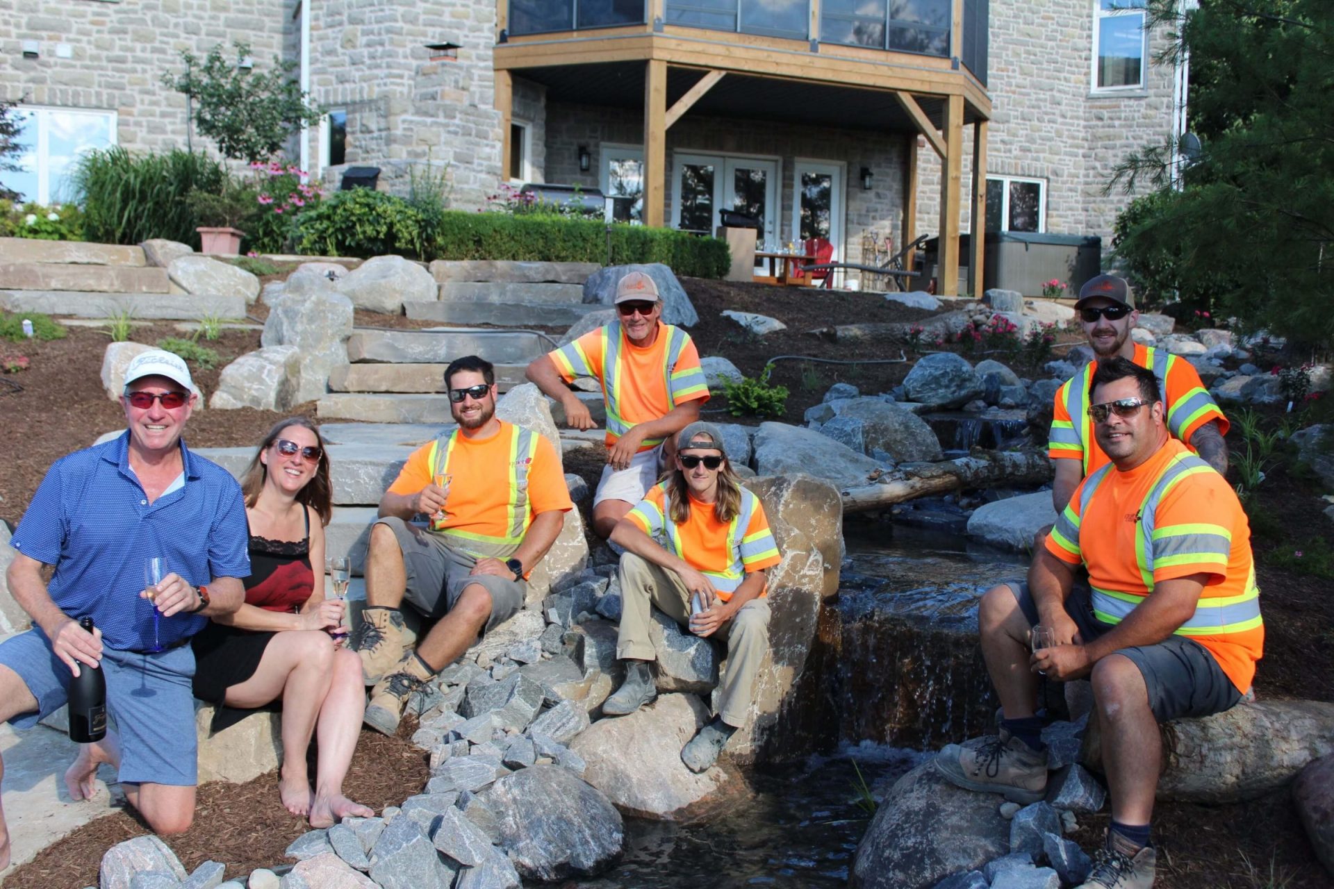 Homeowners and construction crew gathered beside the newly built stream and waterfall during the final stages of the Glen Morris backyard project
