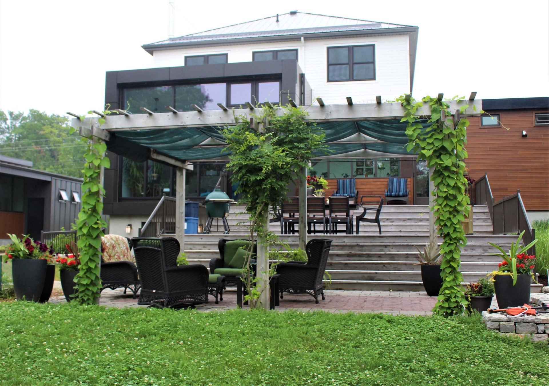 Finished backyard with a pergola-covered seating area, broad wood steps, and outdoor dining space behind a modern home