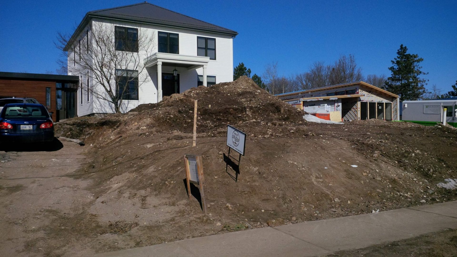 Front view of two adjacent properties with steep exposed grades, raw soil, and unfinished landscaping along the street