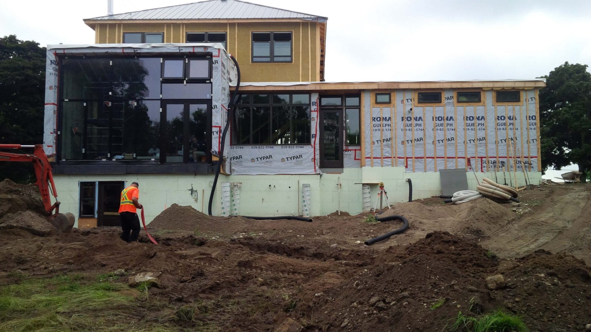 Rear view of a home under construction with exposed soil, rough grading, and unfinished backyard conditions