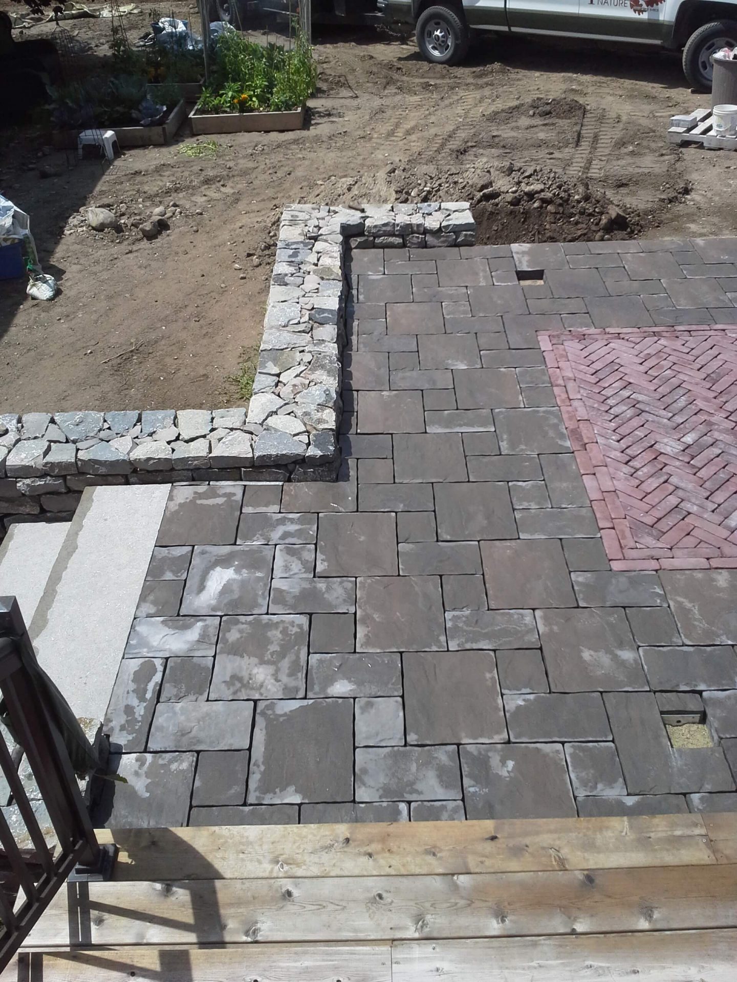 Backyard hardscape under construction with paver patio surfaces, drystone retaining walls, and stone steps taking shape