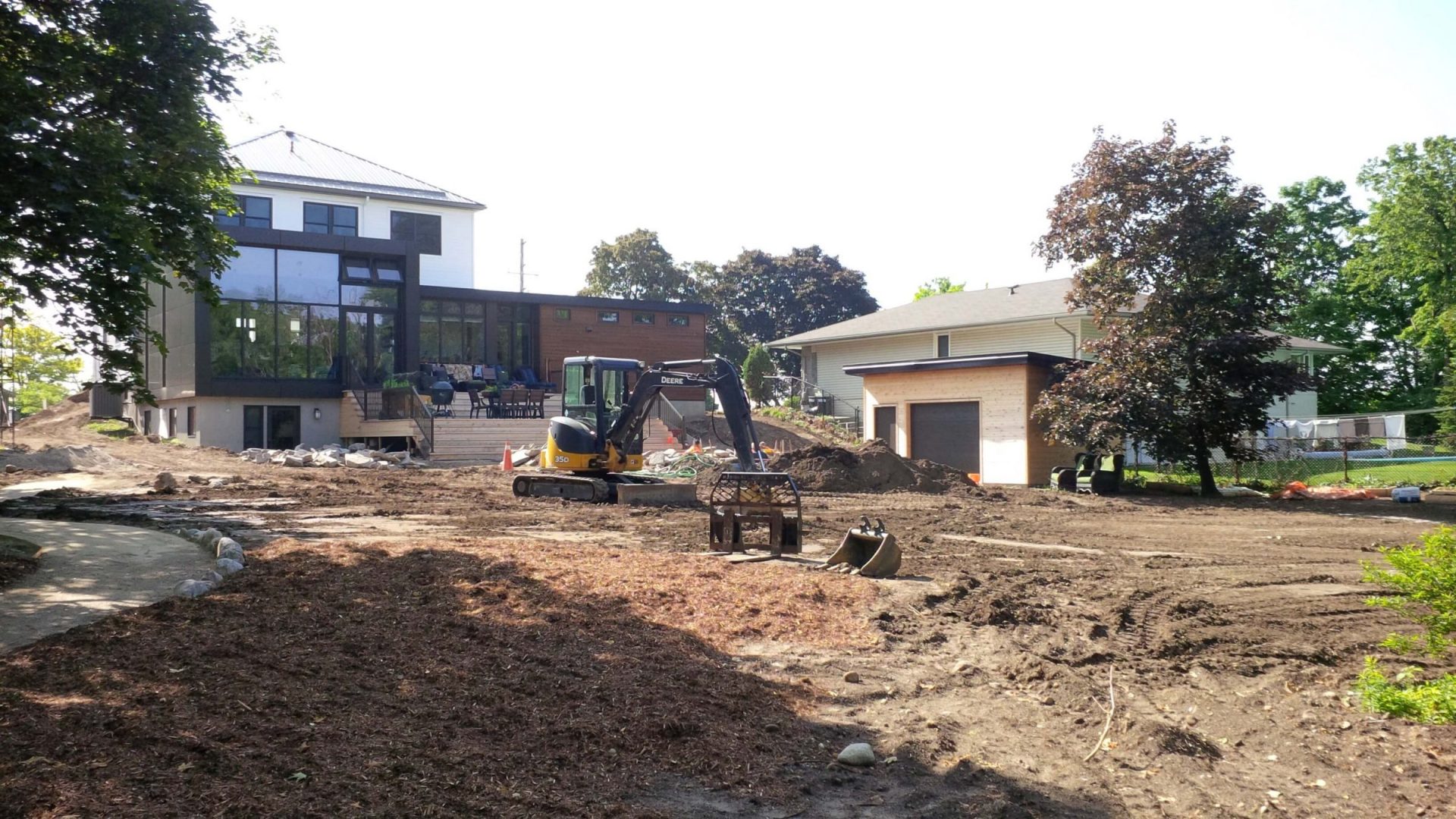 Wide backyard view during construction with excavation work, rough grading, and a modern home and garage in the background