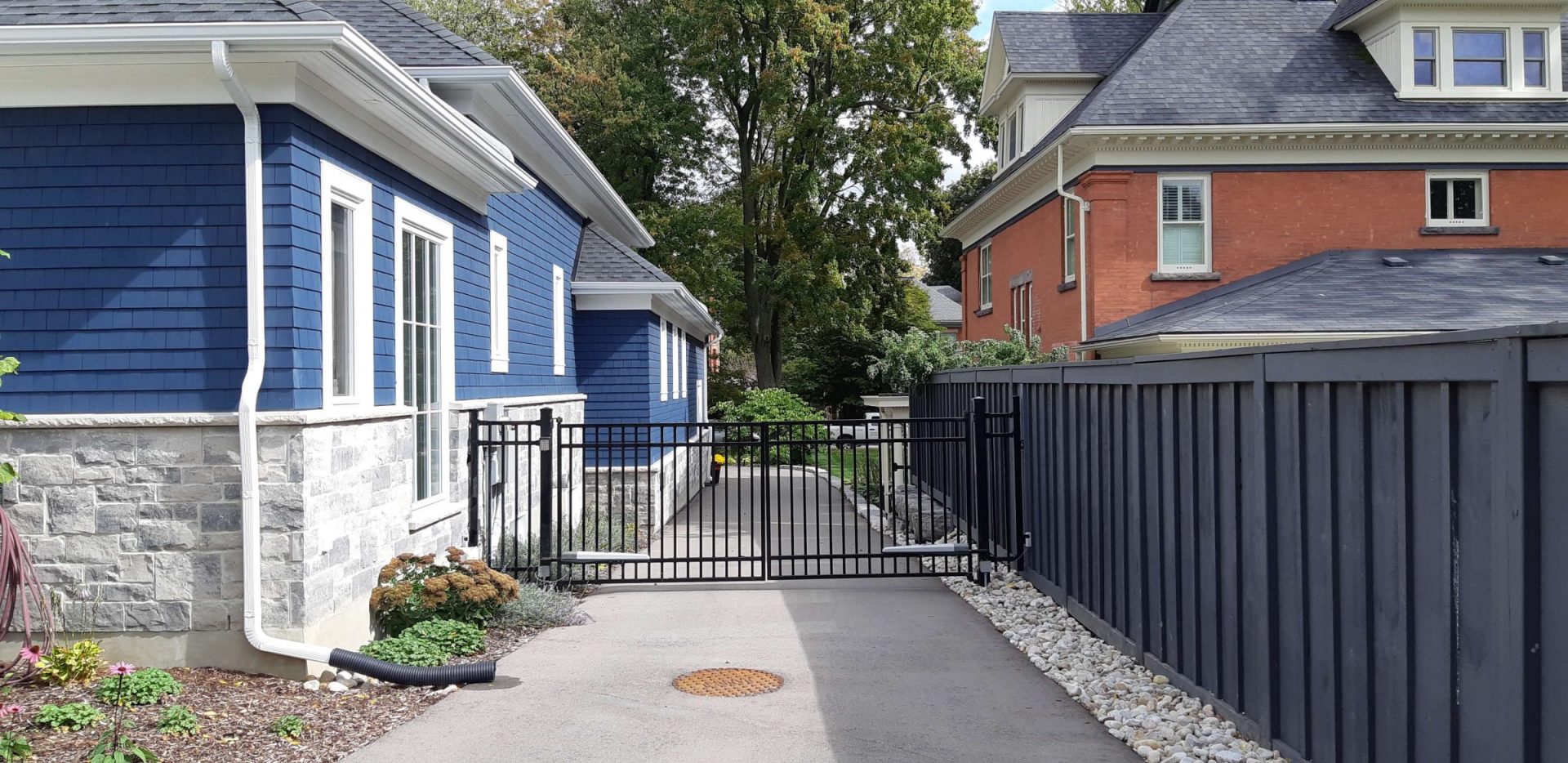 Side yard driveway with a black metal gate, privacy fence, stone foundation, and clean landscaping beside the house