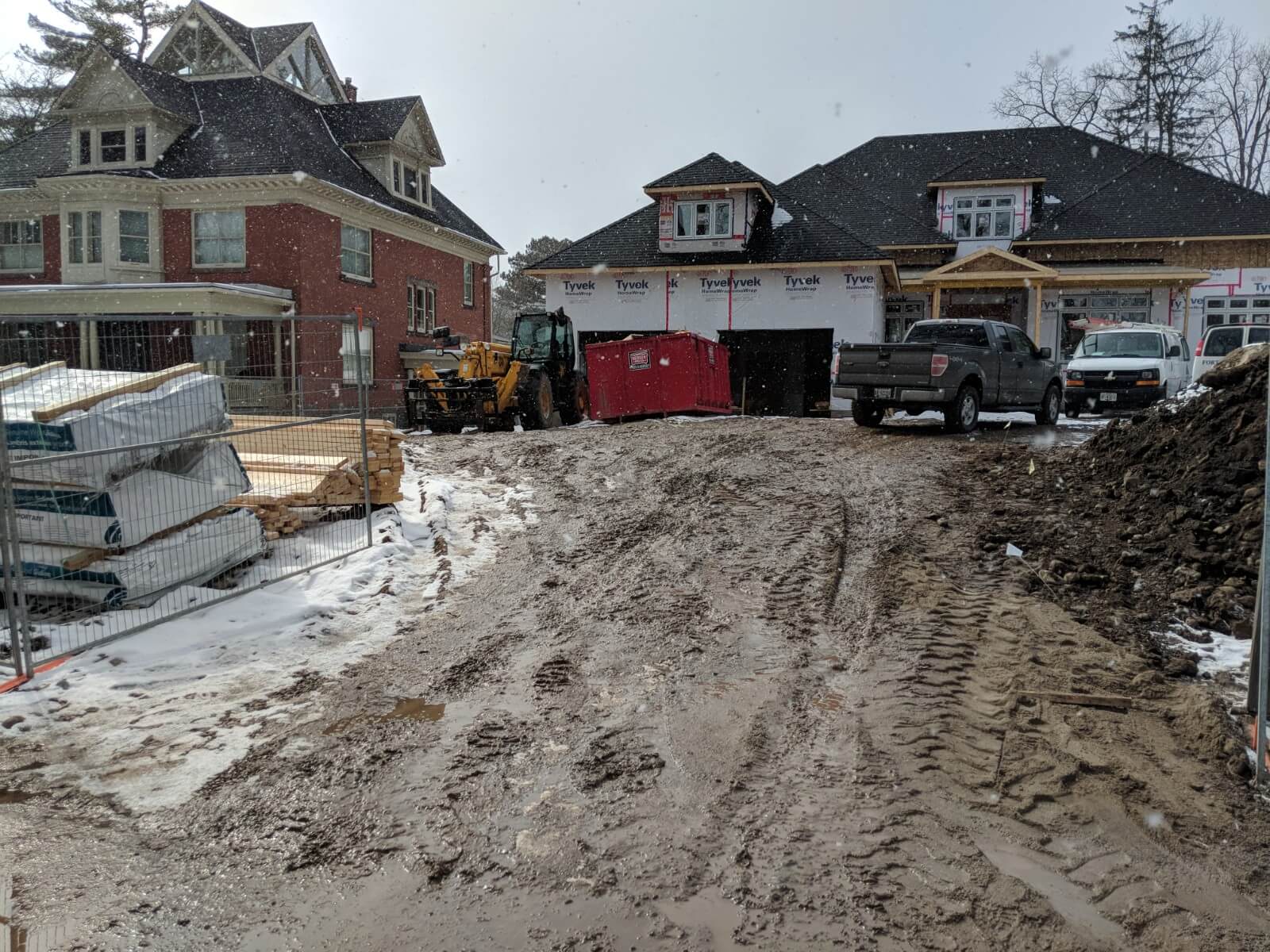 Front entrance area of the house under construction with exposed framing, temporary access planks, and unfinished ground conditions