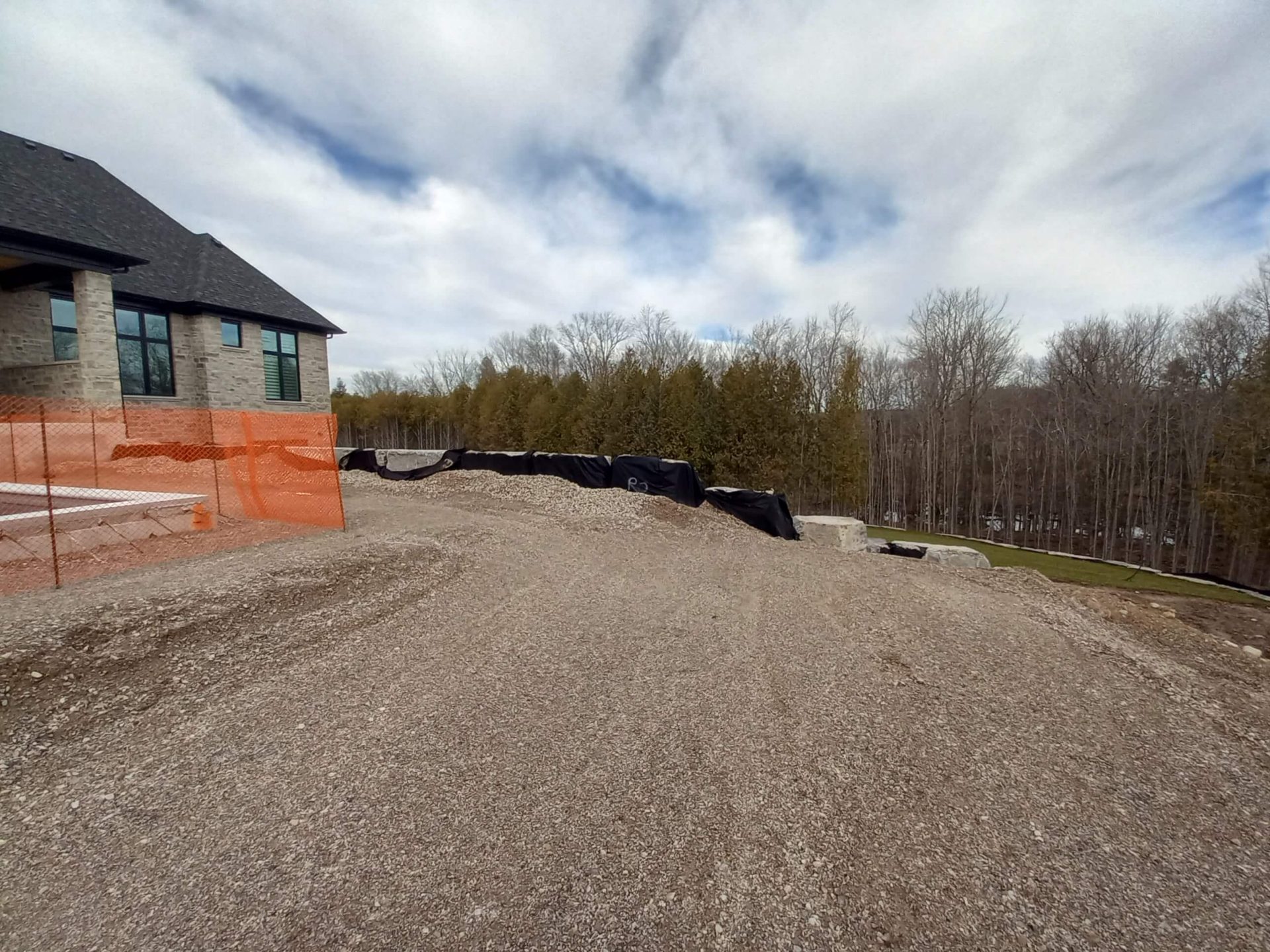 Rear side of the property with rough gravel grading, erosion control fabric, and an unfinished backyard overlooking a wooded slope