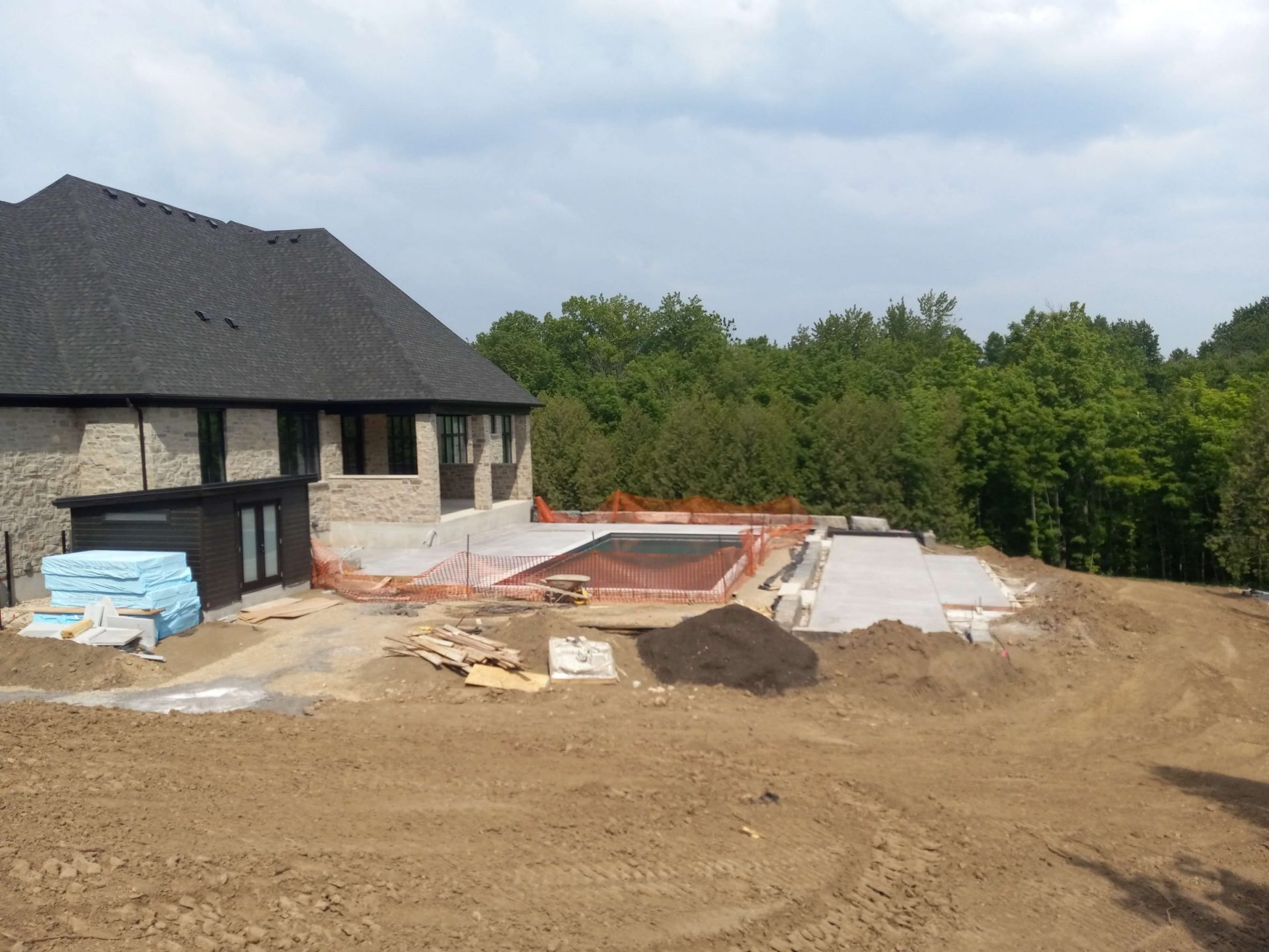 Wide view of the backyard during construction with the pool installed, early concrete patio sections, and rough site grading around the property