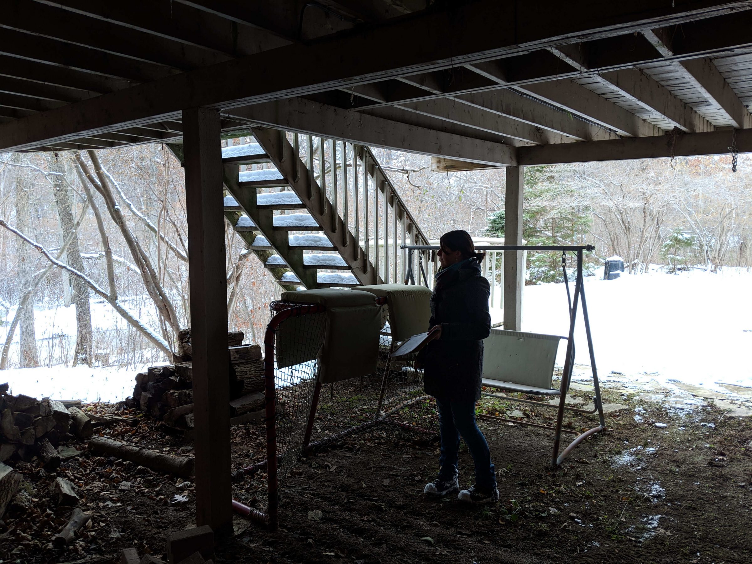 Unfinished area beneath the raised deck with exposed structure, stored items, and an underused backyard space in winter